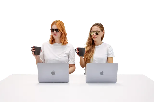 Bild von zwei Personen die an einem Computer arbeiten und dabei mit einer Kaffeetasse in der Hand in die selbe Richtung schauen